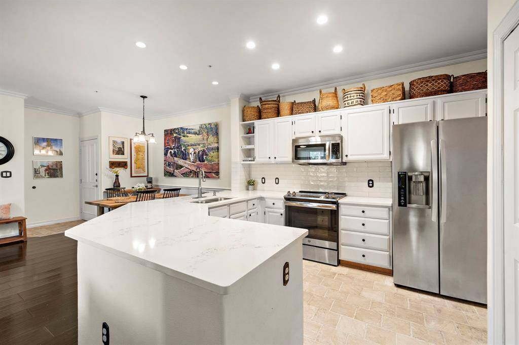 This modern kitchen is well-equipped with updated quartz countertops, stainless steel appliances, a wine fridge, a custom tile backsplash, and seamless access to the dining area.