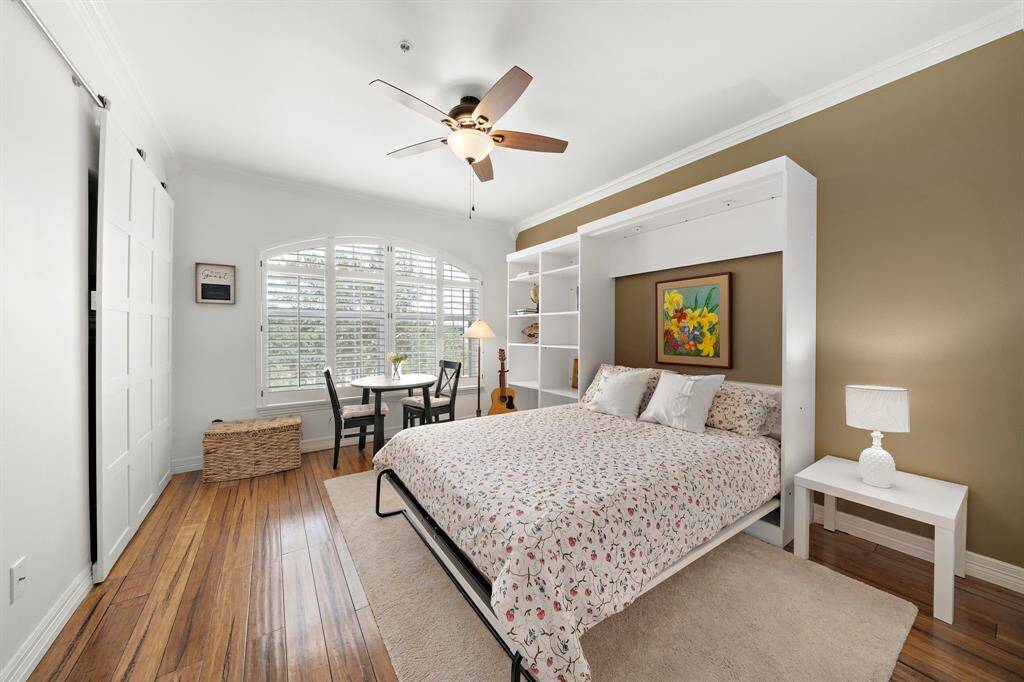 Take respite in the spacious primary suite highlighting an accent wall, crown molding, plantation shutters, and a functional Murphy bed with surround shelving. Enjoy the convenience of a being able to have a sitting area by the large windows that usher in natural light while providing lush outdoor views.
