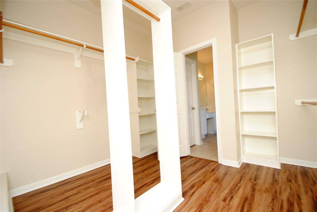 Spacious walk-in closet with wood flooring, ample shelving, and hanging space, leading to a bright bathroom.