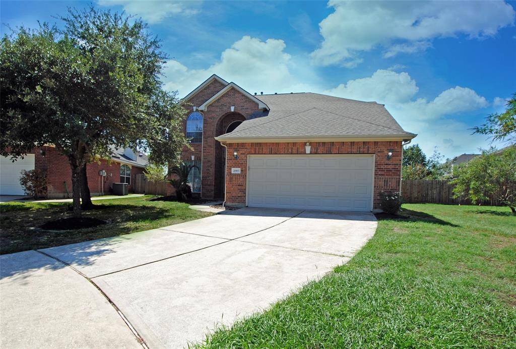 This is a charming two-story brick home with a two-car garage. It features a well-maintained front lawn, a tree providing shade, and a spacious driveway. The property is set in a suburban neighborhood, offering a welcoming curb appeal.