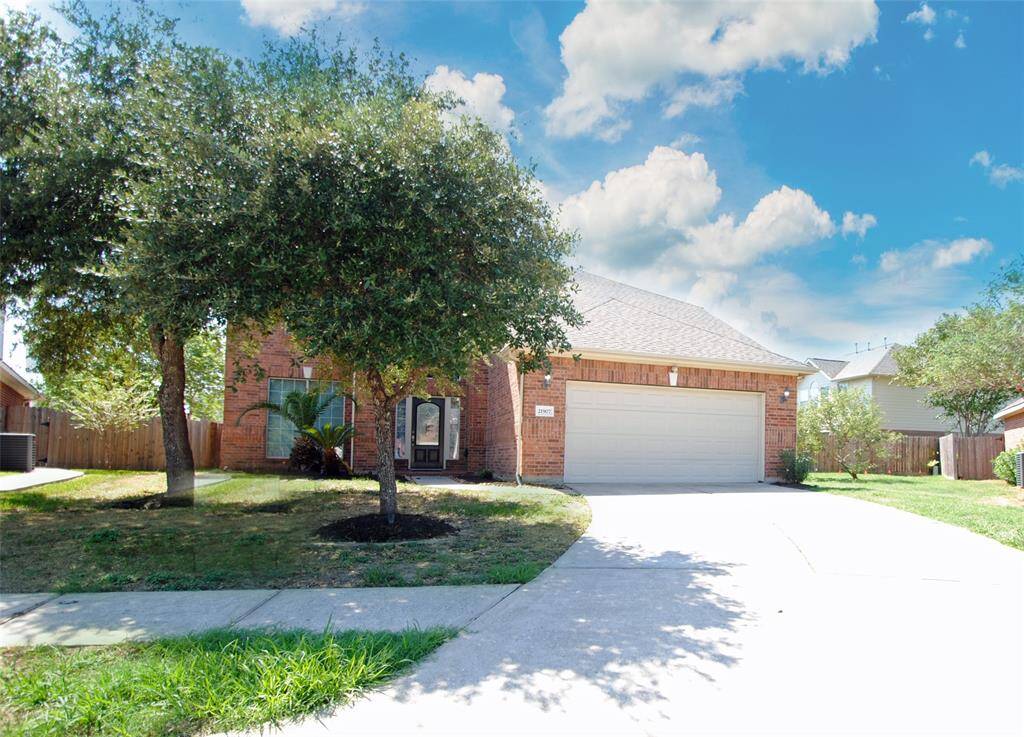 This charming brick home features a well-maintained front yard with mature trees and a spacious driveway leading to a two-car garage. The property has a welcoming entrance and is set against a backdrop of a clear blue sky, offering great curb appeal.