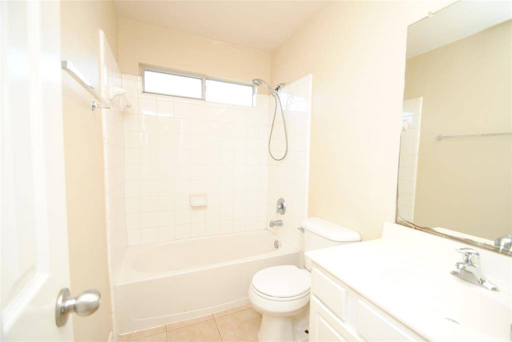 Bright and clean bathroom with a bathtub-shower combo, white tile, and a large mirror above the sink. Compact layout with neutral tones.
