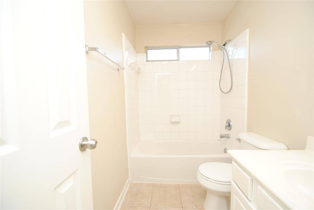 This bathroom features a clean, bright design with a tiled shower and bathtub combo, a window for natural light, a toilet, and a white vanity with storage.