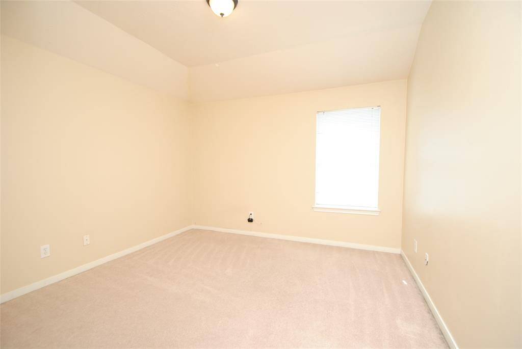 This is a bright, empty room with neutral walls and carpet, featuring a single window and overhead light fixture. Ideal for a bedroom or home office.