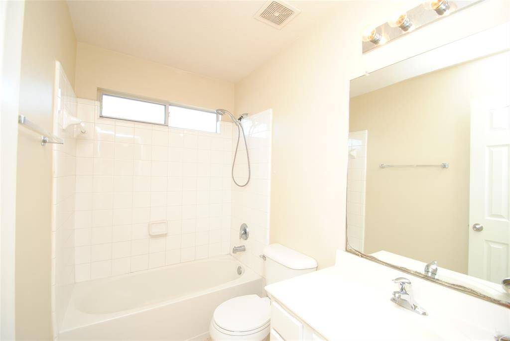 Bright and clean bathroom with a bathtub-shower combo, white tiles, a large mirror, and modern lighting.