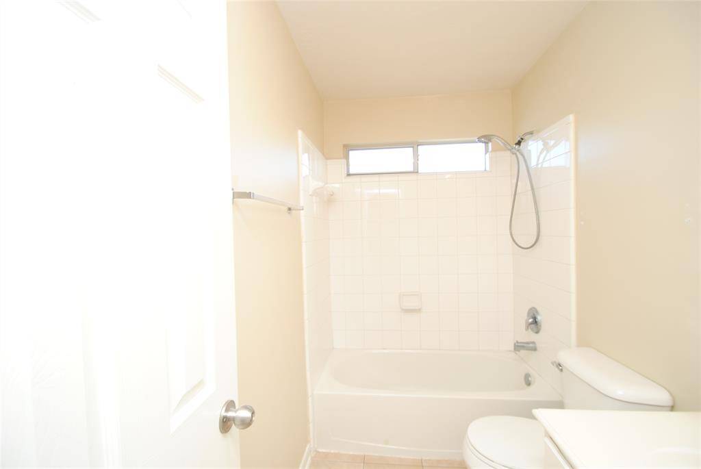 Bright, compact bathroom with a bathtub and shower combo, light tiles, and a window for natural light.