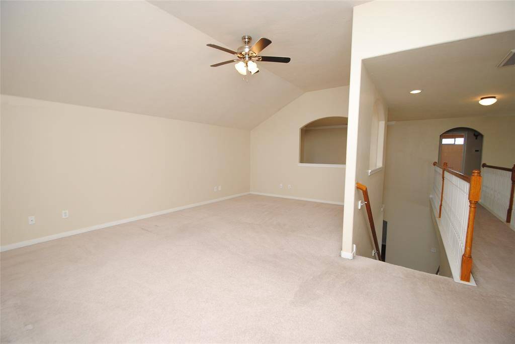Spacious, carpeted loft area with neutral walls, ceiling fan, and recessed lighting. Features open railing overlooking the staircase and a small arched window opening for added character.