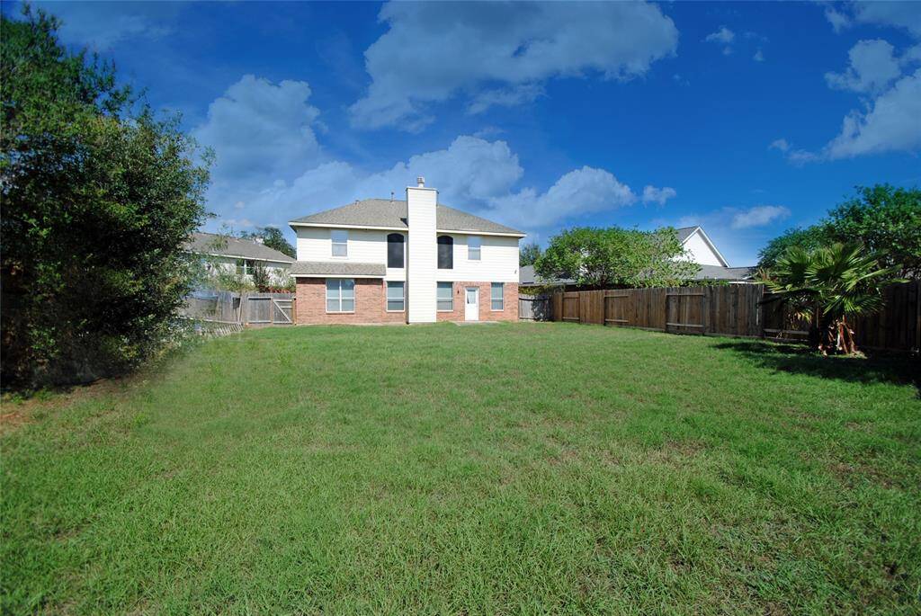 This photo showcases a spacious backyard with a well-maintained lawn, bordered by a wooden fence. The two-story house features a mix of brick and siding, with several windows and a central chimney. Perfect for outdoor activities and family gatherings.