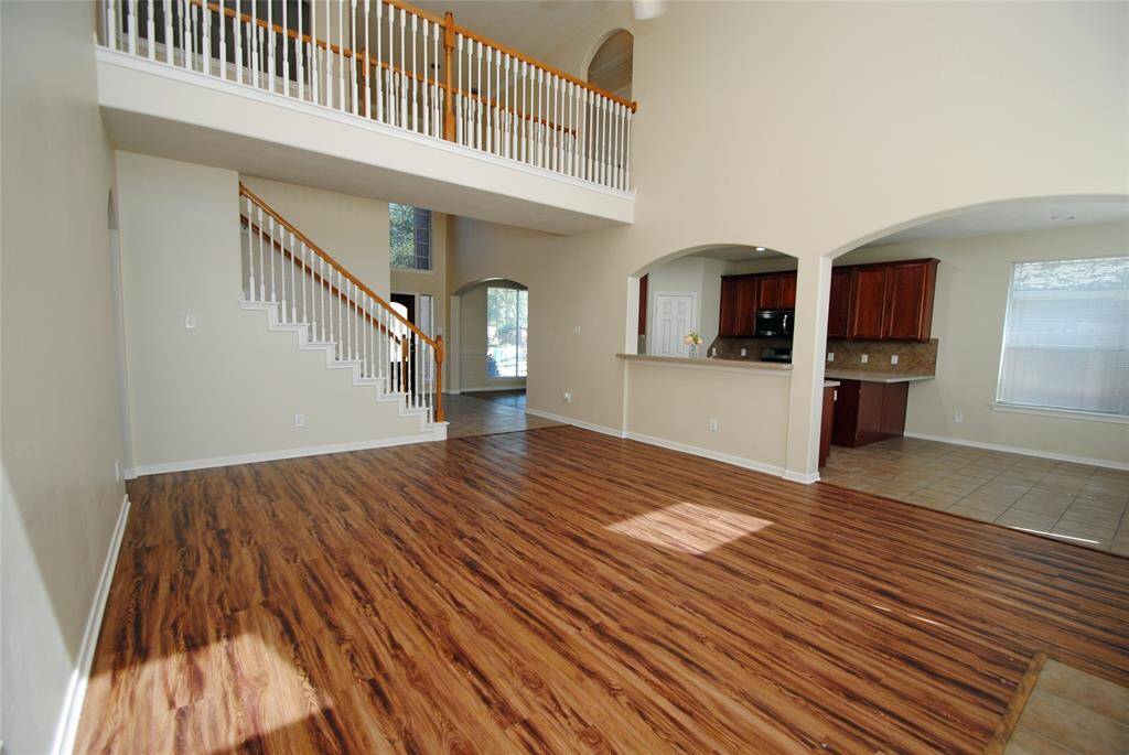 This spacious living area features high ceilings, a beautiful wood floor, and an open layout with a view of the upper loft. The adjacent kitchen has tile flooring and modern cabinetry, creating a warm and inviting atmosphere.