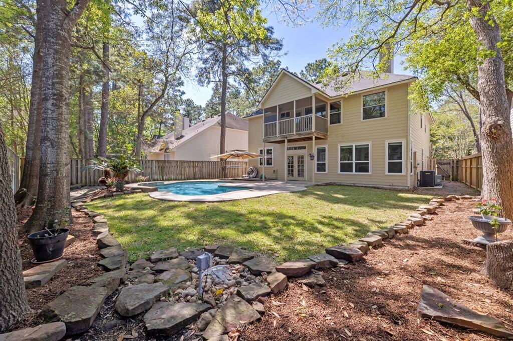 This backyard showcases a spacious two-story home with a fenced yard, featuring a pool accented by surrounding trees and landscaped stone pathways, perfect for outdoor relaxation and entertainment.