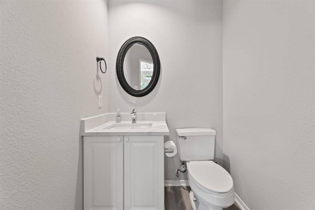 This bathroom features a modern design with a sleek white vanity, a round mirror, and a toilet. The neutral color scheme and simple decor create a clean, bright space.