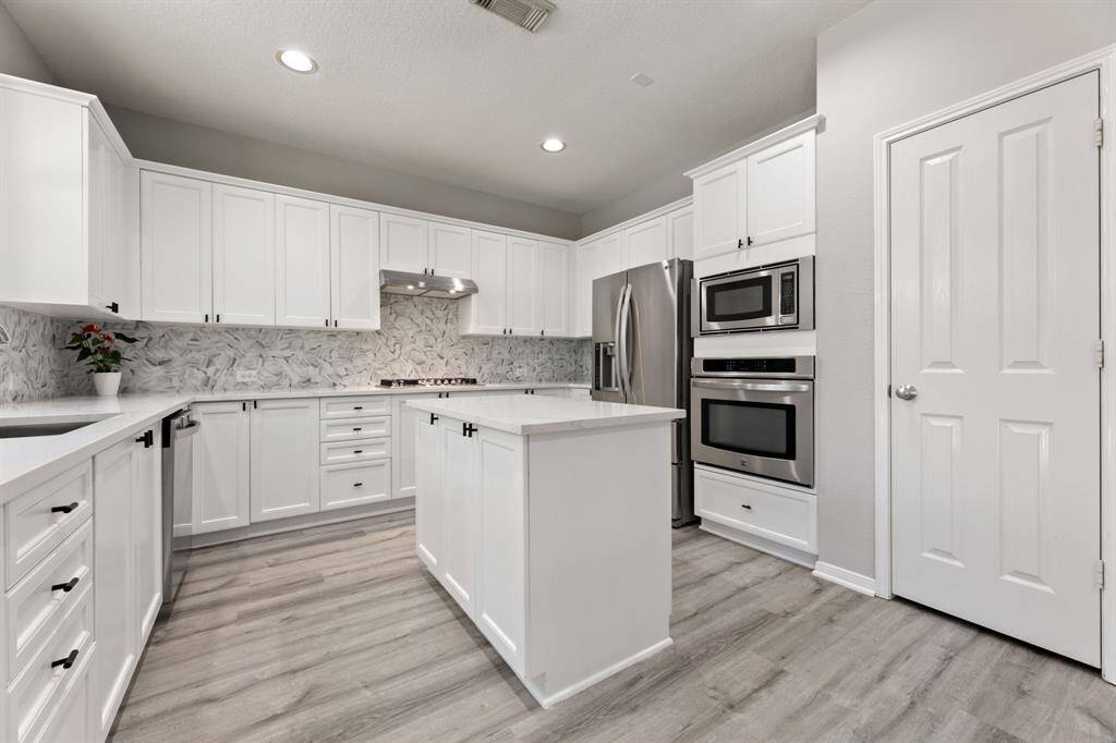 The marble-patterned backsplash adds elegance, while the wood-look flooring provides a warm touch. Ample storage and a bright atmosphere make it inviting.