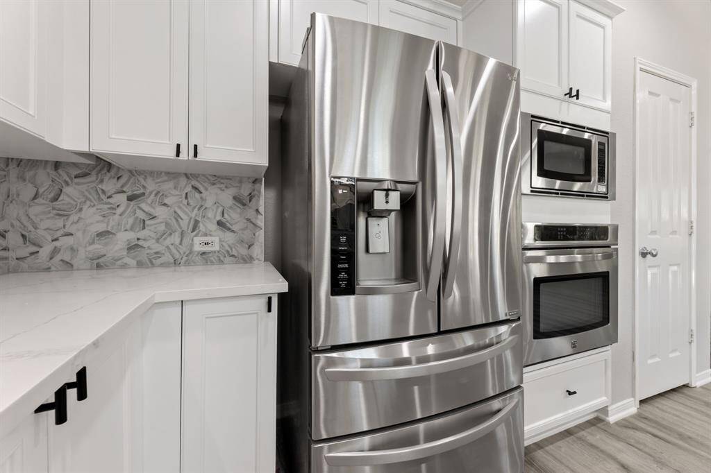 Modern kitchen with a French-door refrigerator and built-in microwave. White cabinetry and a stylish gray backsplash add elegance, while light countertops provide a clean, bright look.
