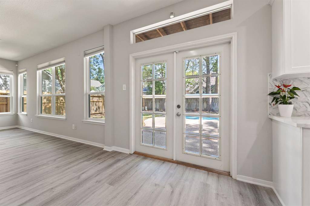 Bright and inviting family room with large windows and glass double doors leading to a backyard with a pool view. The space features light wood flooring and modern finishes, creating an open and airy atmosphere.