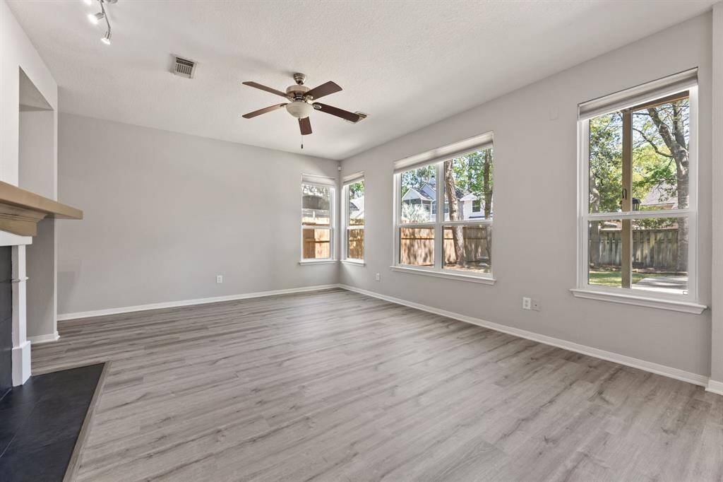 Bright and spacious Family room with large windows, light gray walls, and wood-style flooring. Features a ceiling fan and a cozy fireplace.