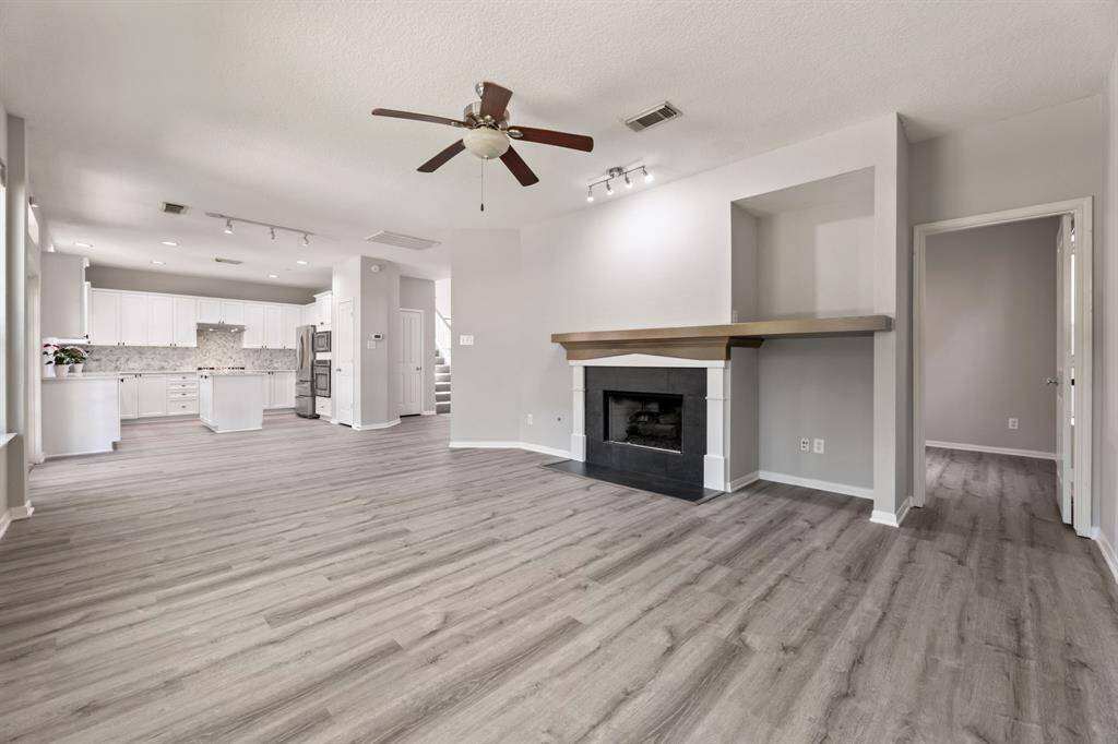 This spacious open-concept living area features sleek hardwood floors, a cozy fireplace with a modern mantle, and a ceiling fan. The adjoining kitchen is bright and contemporary, with white cabinetry and stainless steel appliances, perfect for entertaining.