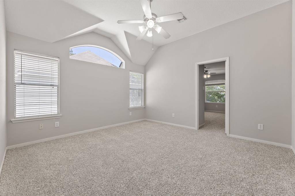 It features a ceiling fan, two windows with blinds, and a distinctive arched window. An open doorway leads to an adjacent room.