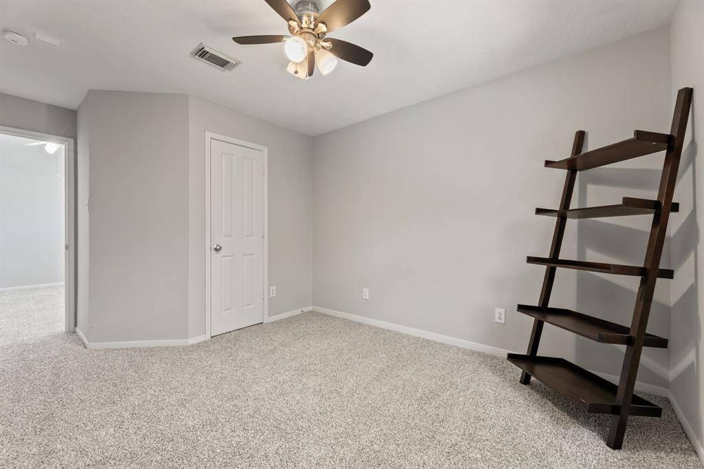 A cozy, carpeted room with neutral gray walls, a ceiling fan, and a built-in closet. It features a modern, dark wood leaning shelf, offering a versatile space for a bedroom or  another office upstairs.