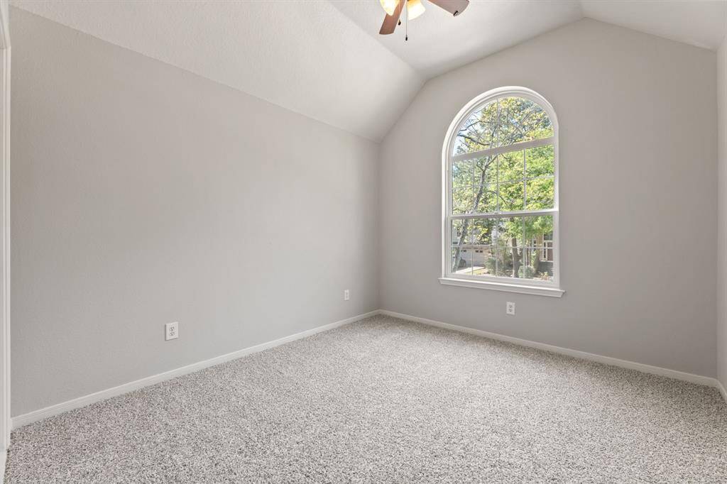 This room features a vaulted ceiling, a large arched window offering plenty of natural light, neutral gray walls, and plush new carpeting, creating a bright and welcoming space.