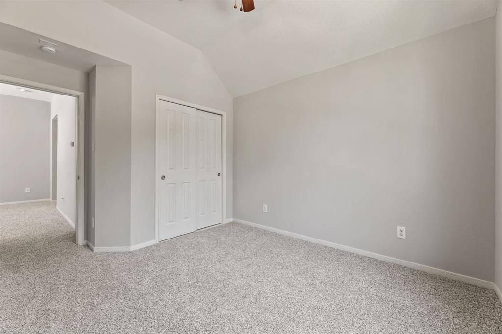 This bedroom features neutral-toned walls and carpet, a sloped ceiling, and a double-door closet, offering a spacious and versatile interior.