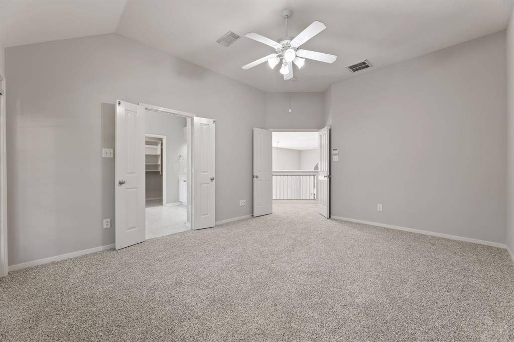 Spacious, new carpeted room with neutral walls, a ceiling fan, and double doors leading to another area, perfect for a bedroom.