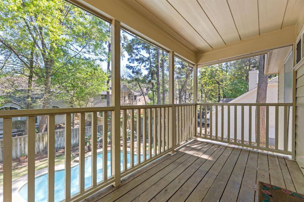 This photo showcases a cozy screened-in porch with wooden flooring, offering a serene view of lush trees and a backyard pool. Perfect for relaxation and enjoying outdoor scenery.