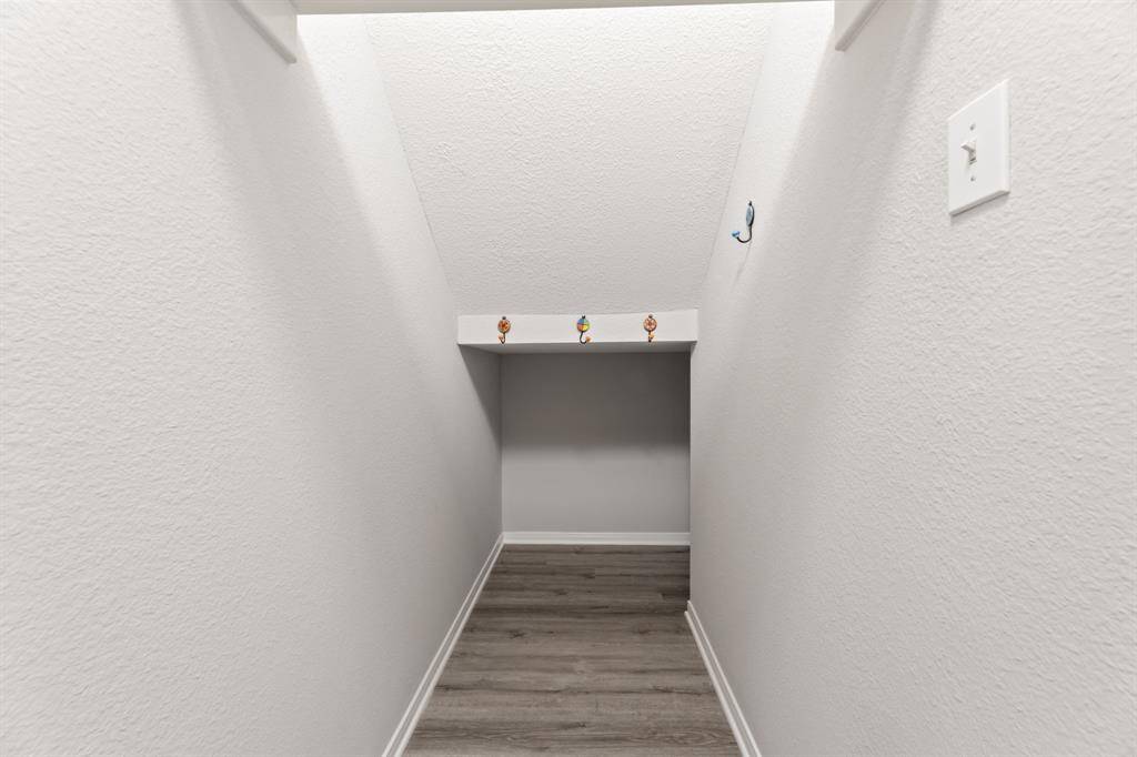 This photo shows a small, angled storage nook with light-colored walls and wood flooring. It features decorative hooks and a recessed shelf, ideal for additional storage or creative use.