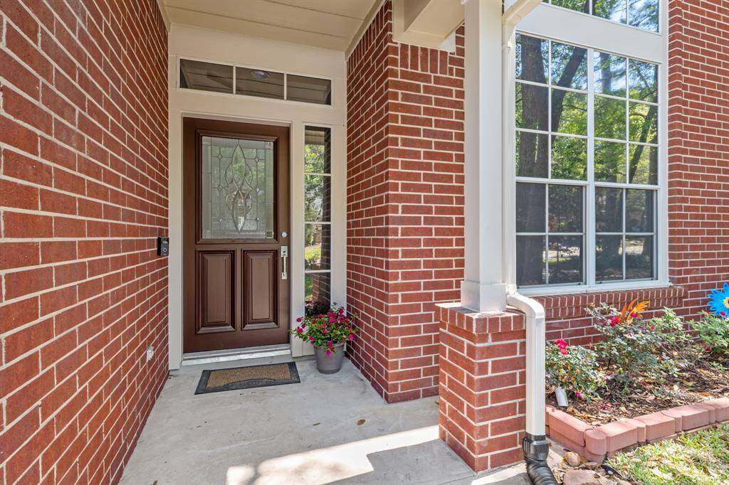Charming brick entryway with a decorative glass front door and large window, surrounded by a small garden with vibrant flowers. Perfect for welcoming guests.