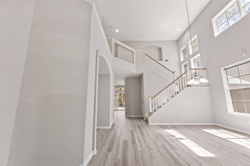 This photo showcases a bright, spacious entryway with high ceilings, large windows, and a modern staircase.