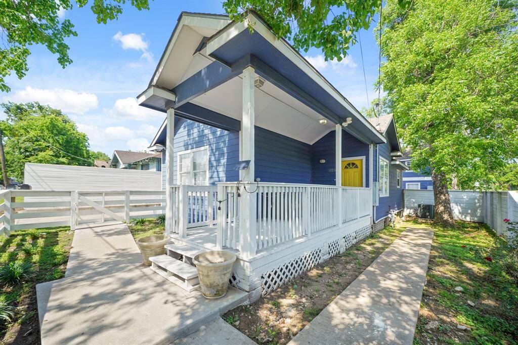 Charming blue exterior front unit with white trim, featuring a welcoming front porch and a spacious concrete driveway. Surrounded by lush greenery, it offers a cozy and inviting atmosphere on a corner lot.