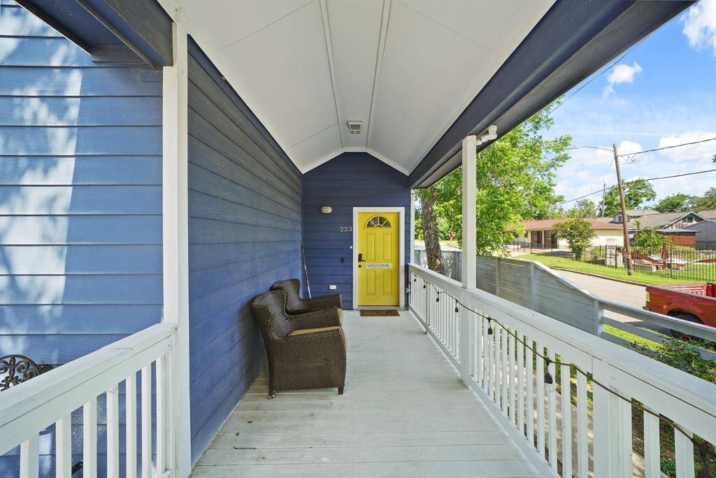Charming blue exterior front unit with a welcoming front porch and vibrant yellow door. It features a white fence and pathway, shaded by mature trees, offering a cozy and inviting entrance.