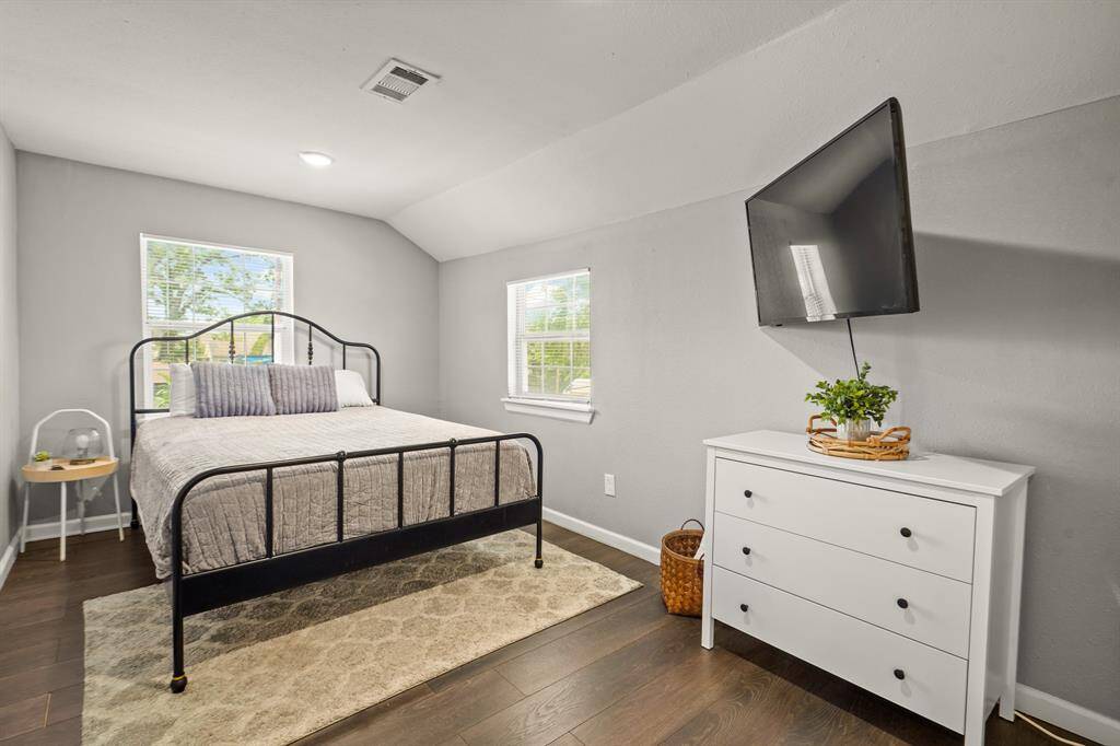 An open-concept kitchen and living area. The kitchen features dark cabinetry, granite countertops, and stainless steel appliances. The adjacent living room is bright, with a large window, ceiling fan, and modern furnishings. The space has hardwood floors and a cozy, inviting atmosphere.