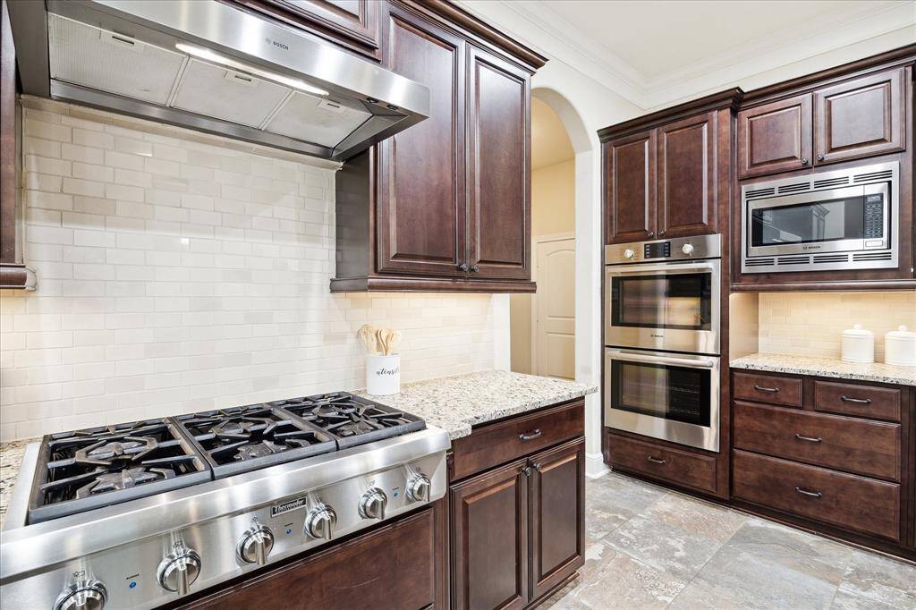 Close up of Thermador 6 burner cooktop, double oven and microwave.  Hallway leads to stairs, guest bath and garage.