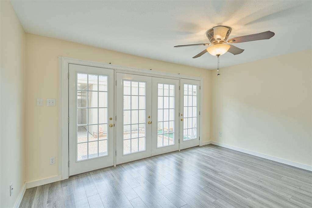 Bright and spacious room with wood-look flooring, a neutral palette, and a ceiling fan. Three French doors flood the space with natural light and lead to the outdoors.