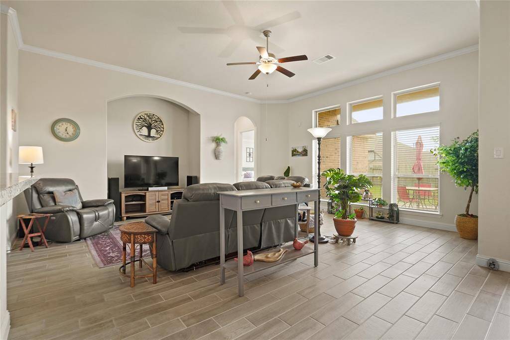 This spacious living room features abundant natural light from large windows, a ceiling fan, and a cozy seating area perfect for relaxation. The open layout is complemented by a view of the patio, creating an inviting atmosphere.