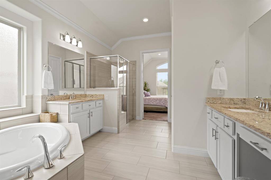 Indulge in the luxurious primary bathroom, featuring a serene soaking tub, elegant tiled shower, and dual sinks with a convenient vanity area.