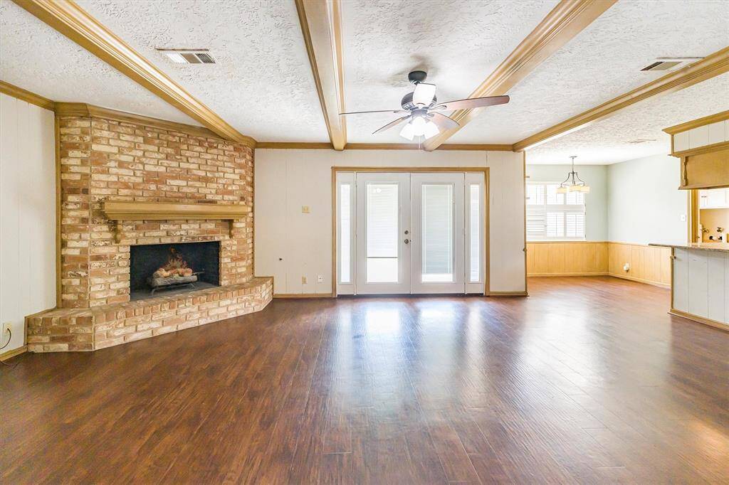 Large living space with cozy brick fireplace, attractive wooden beams and french doors leading to the patio in the backyard.