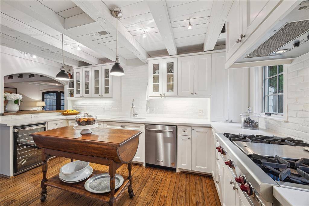 The wood beamed ceilings continue into the kitchen where custom cabinetry and painted brick backsplash give this a California or Hampton's style. The center island is an antique dough table that will remain with the home. Lighting pendants and the wine refrigerator are great features.