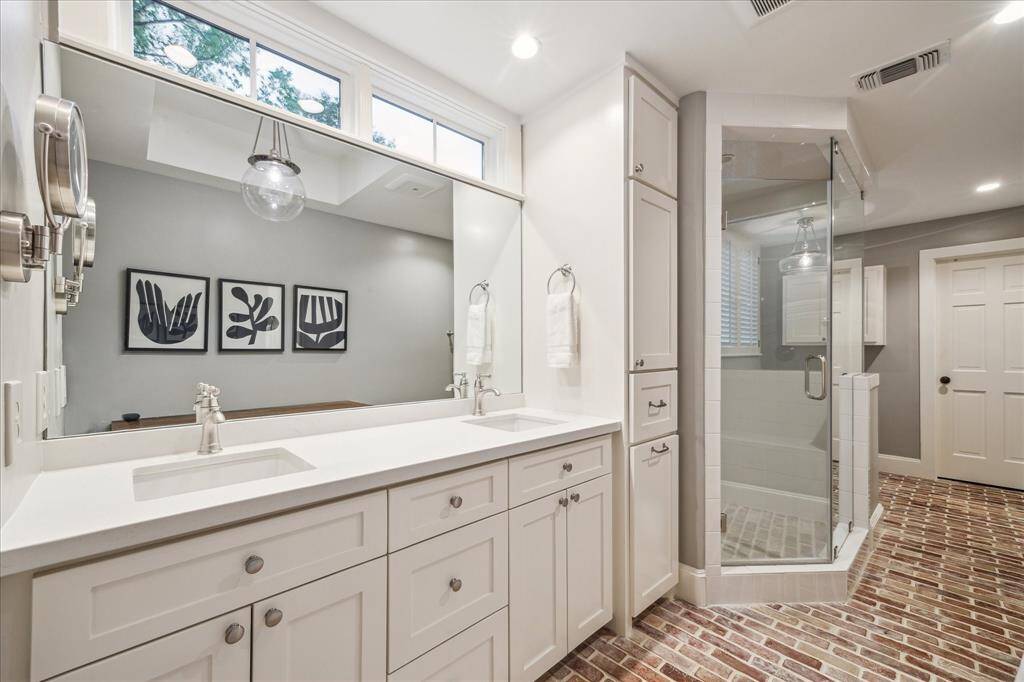 This large Primary Bathroom has double sinks with transom windows above for natural light, brick flooring, walk-in shower and a soaking tub.