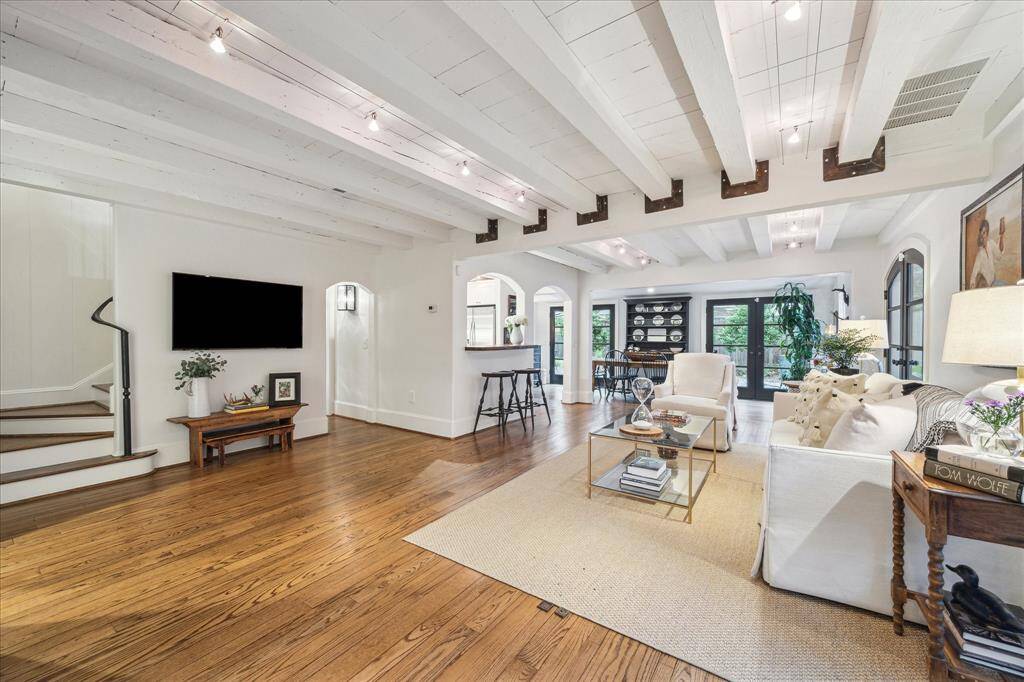 Another wider view with gleaming hardwood flooring, television, staircase, breakfast bar and dining room beyond.