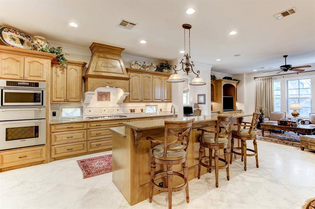 A close up of the kitchen focusing on the island with breakfast bar, gas range, stainless ovens, abundant cabinet storage and gas range.