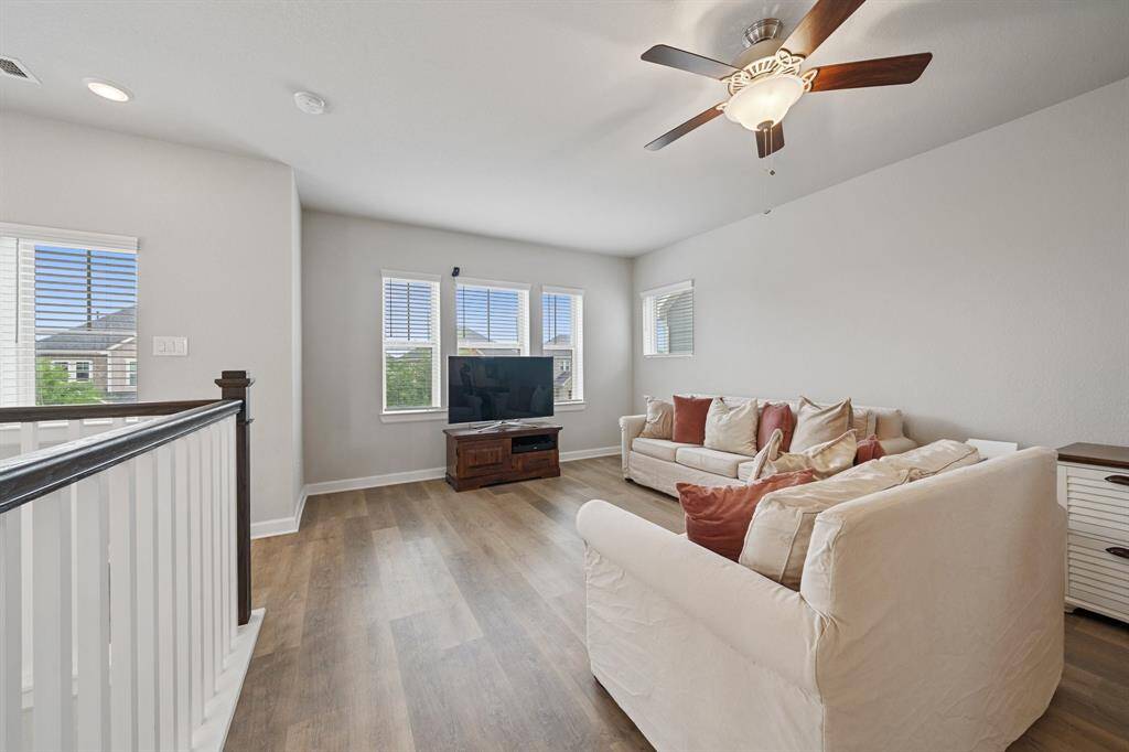 The upstairs game room is designed for both fun and function, featuring luxury vinyl plank flooring, a ceiling fan, and multiple windows with privacy blinds that fill the space with natural light.