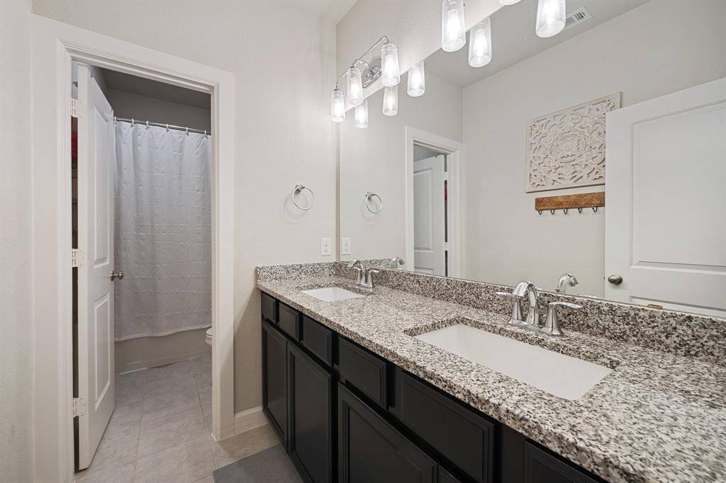 This stylish bathroom offers a practical layout with a separate shower/tub combo and toilet area, plus a double sink vanity featuring dark cabinetry and a sleek granite countertop—perfect for both convenience and elegance.