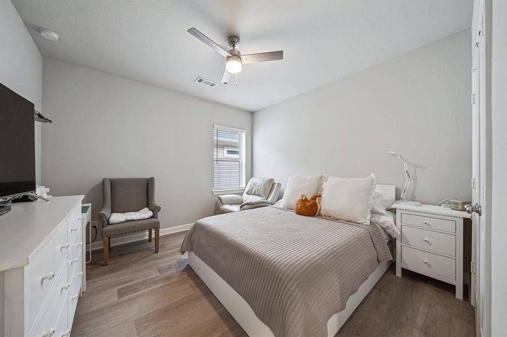 This cozy bedroom features luxury vinyl plank flooring, a ceiling fan for comfort, and a window with privacy blinds, offering both style and functionality.