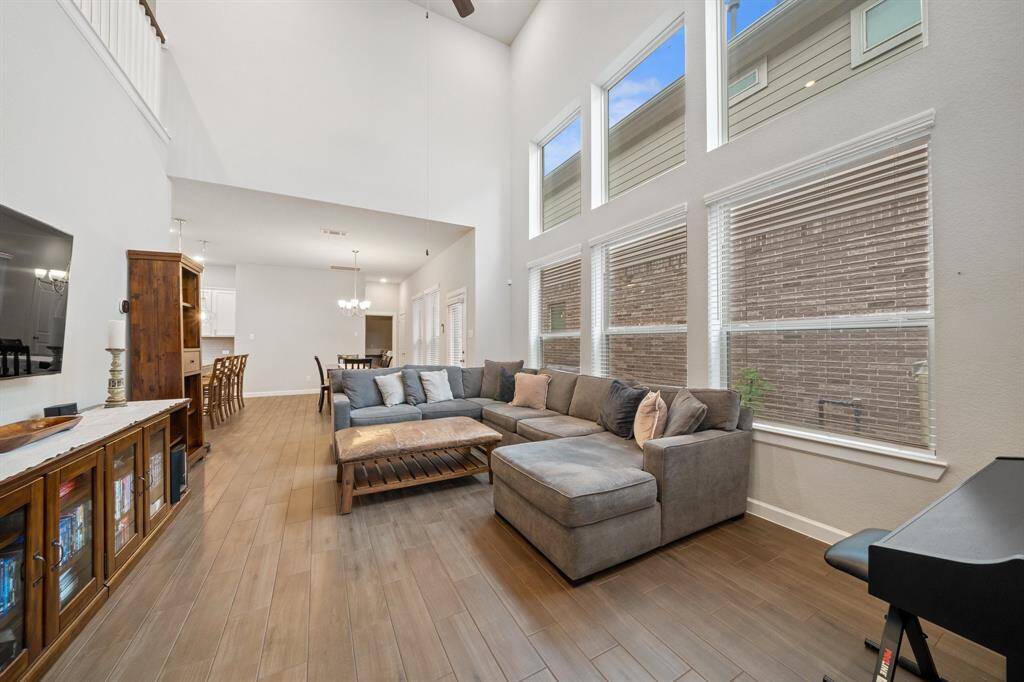 This spacious living room features soaring high ceilings, beautiful wood-look tile flooring, and a stunning wall of windows with privacy blinds that fill the space with natural light.