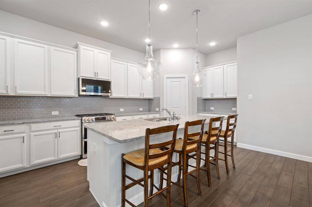 The kitchen boasts sleek white cabinets, elegant glass light fixtures, a functional island perfect for prep or gathering, and recessed lighting that adds a modern touch.