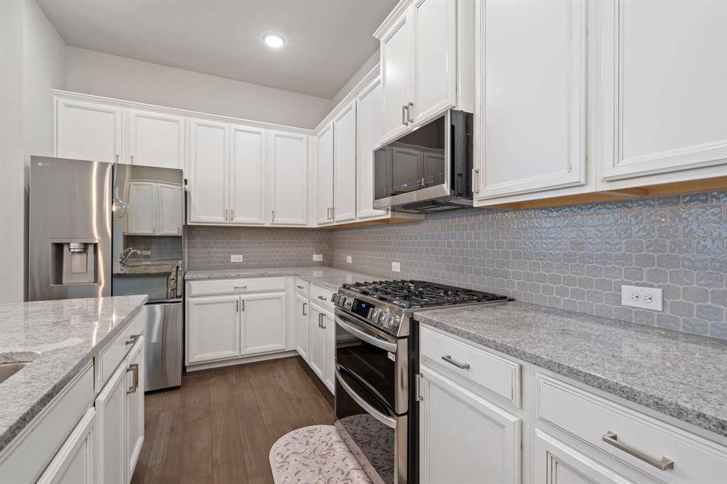 This close-up view highlights the stunning custom back-splash, luxurious granite counter-tops, and sleek stainless steel appliances that elevate the kitchen’s modern design.