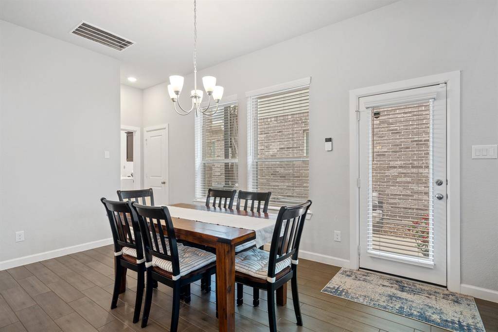 The dining area features elegant wood-look tile flooring, a stylish chandelier, and windows with privacy blinds, plus convenient access to the side yard for seamless indoor-outdoor entertaining.