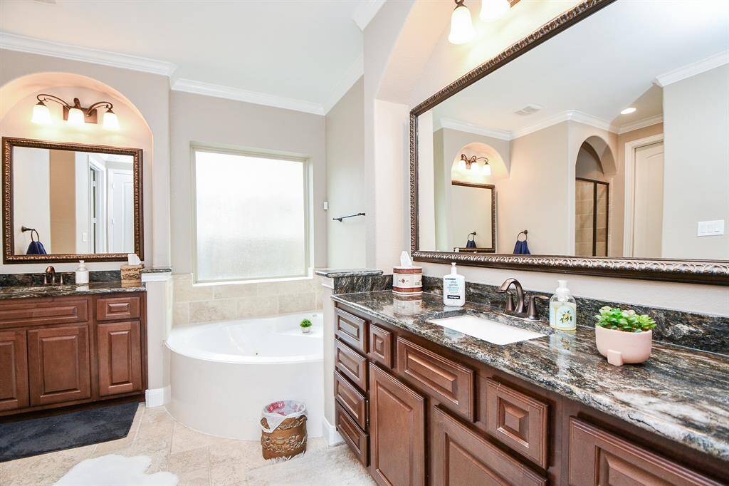The primary bathroom features tile floors, dual sinks, wood cabinets, dark cabinets, walk-in shower, large frosted window, and separate soaking tub.