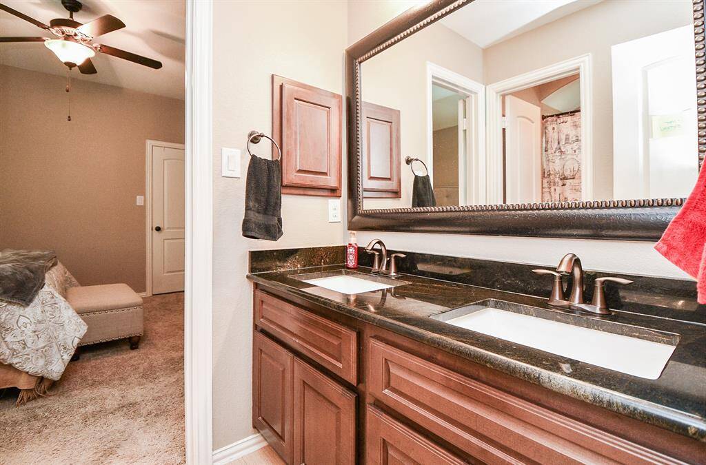 The secondary bedroom also has an en-suite bathroom with dual sinks, dark counters, and wood cabinets.